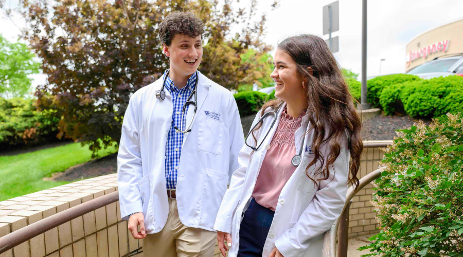 two students in white coats walking around hospital