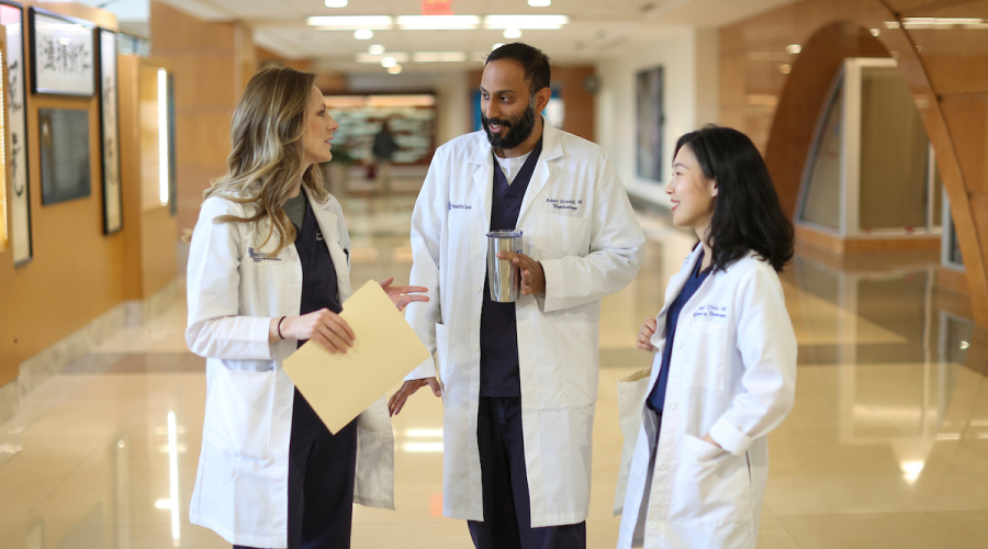 3 residents stand and talk to each other wearing white coats