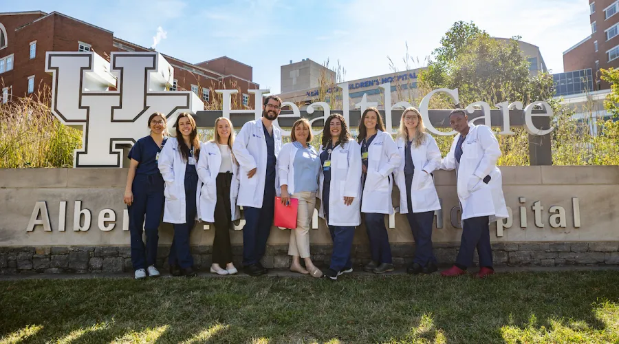 a group of uk college of medicine residents in scrubs and white coats stand in front of the uk chandler hospital