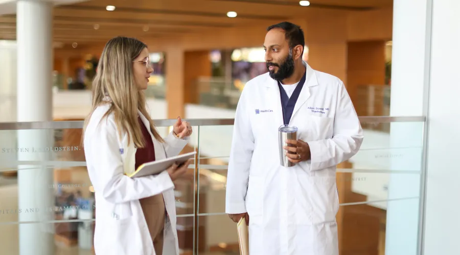 two doctors smile at one another in a brightly lit hallway