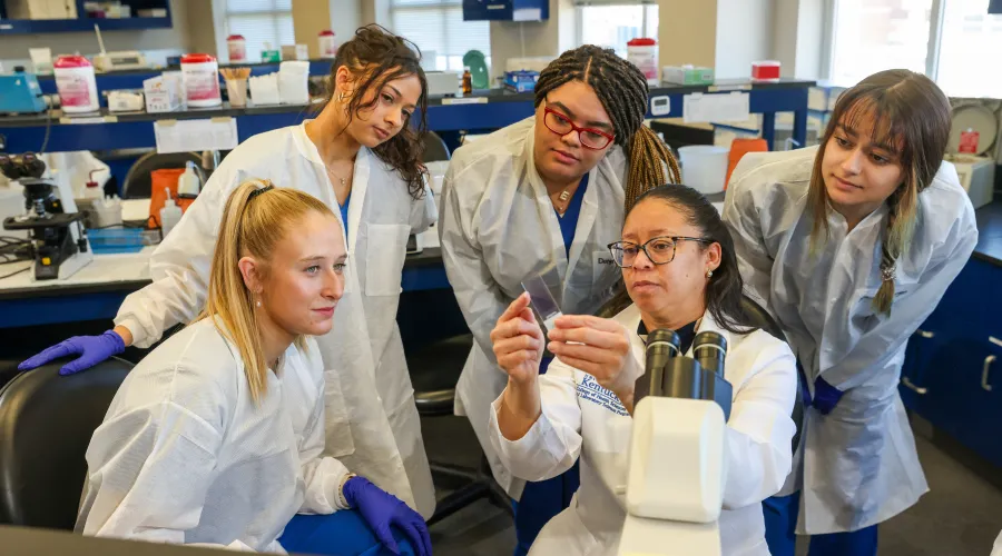 A group of people look at a piece of lab equipment, held up by a woman