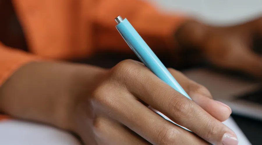 A hand writes with a blue pen in a notebook