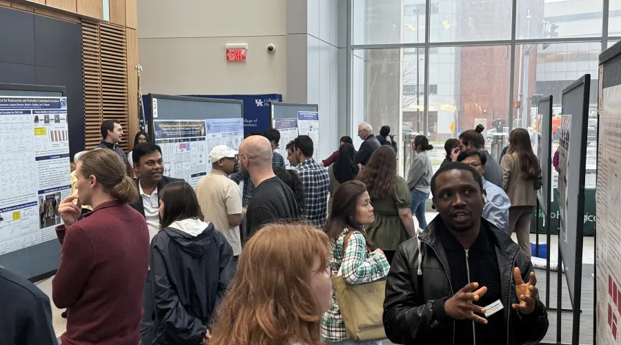 Trainees and researchers fill a bright atrium lined with scientific posters, talking in small groups and presenting their work during the Infectious Diseases Research Day 2025 poster session at the University of Kentucky.