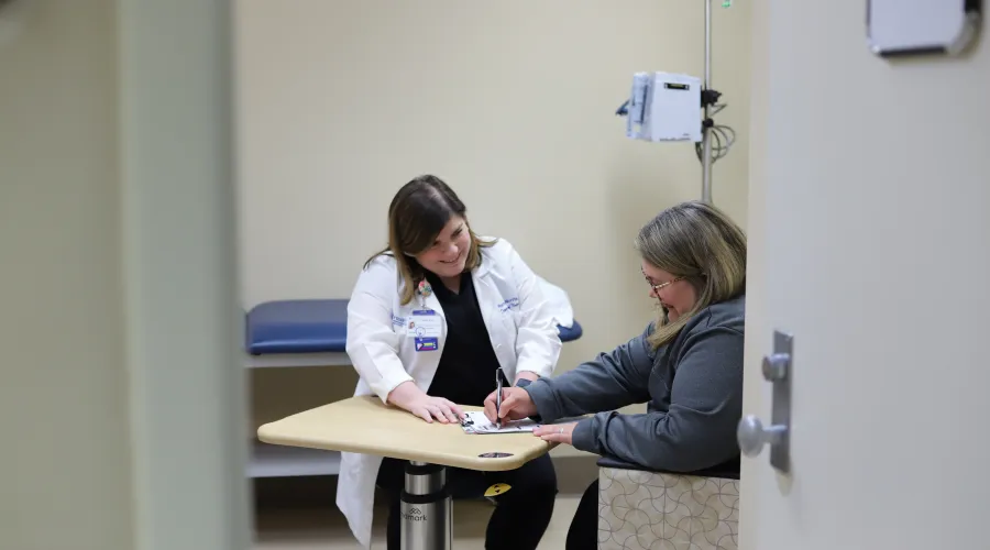 research professional sits in an exam room with patient as they discuss a piece of paper