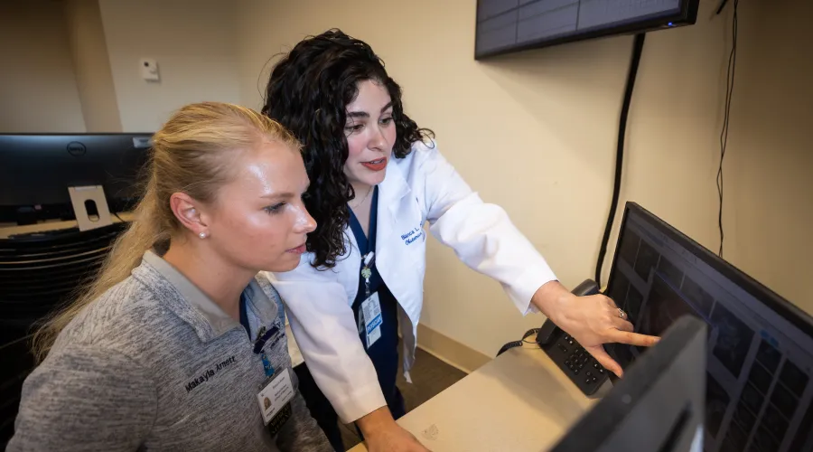 A female student being guided through a computer process by a woman in a white coat.
