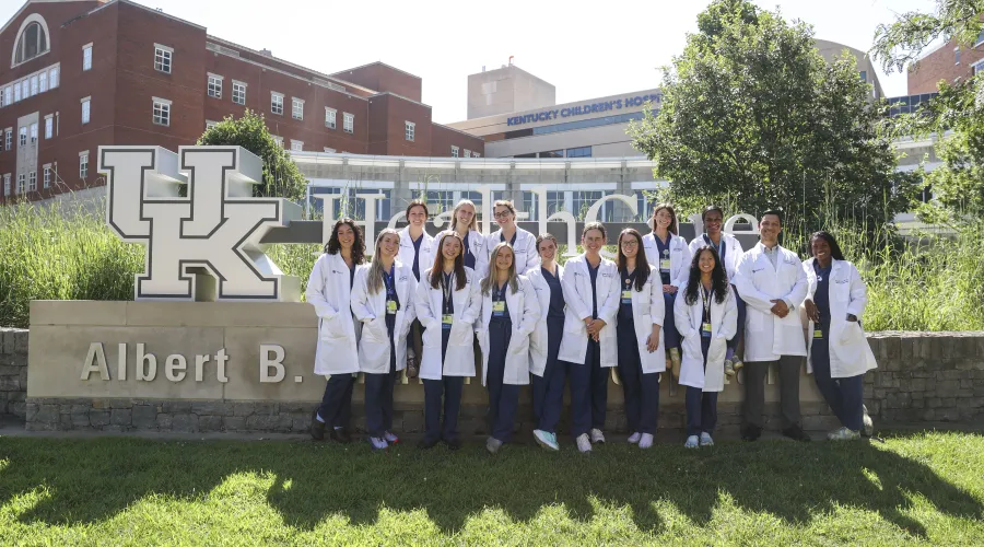 Group of medical professionals standing in front of UK HealthCare sign with hospital in background