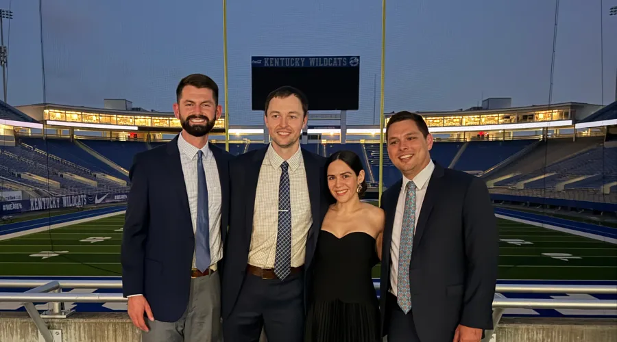 Four residents in formal attire, standing above the UK football stadium.