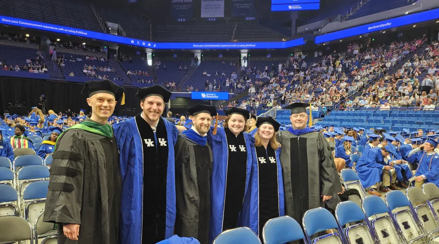 six people standing in a row wearing graduation caps and gowns in an arena