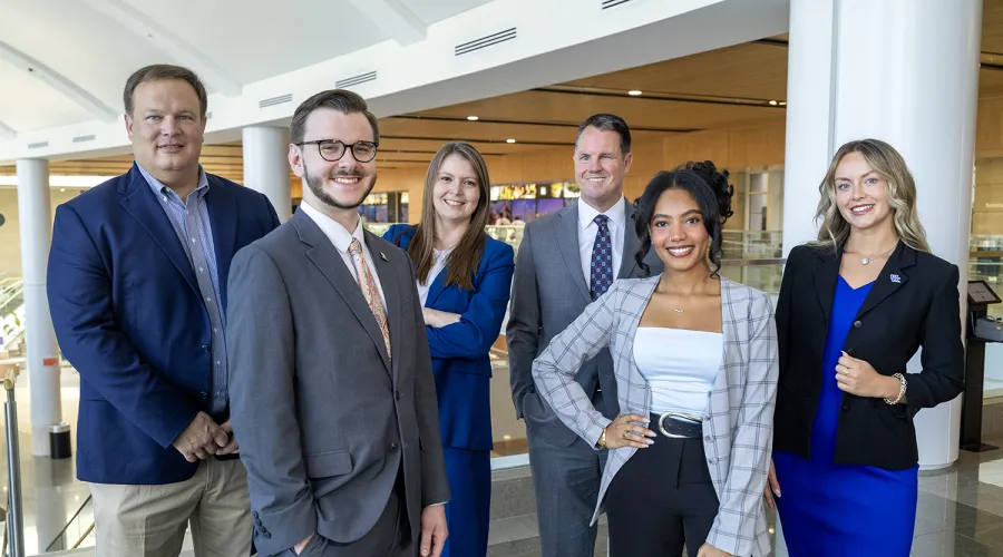 A group of six professionally dressed men and women standing together in the bright, modern lobby of Albert B. Chandler hospital.