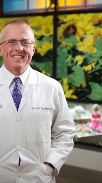 Scottie Day, MD, poses by the Kentucky Wall outside KCH, with both hands in the front pockets of his white coat