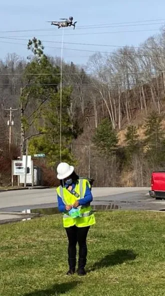 Chyna Smith, left, and Carole Frazier standing outdoors, wearing reflective safety vests as they retrieve a package delivery from a drone.