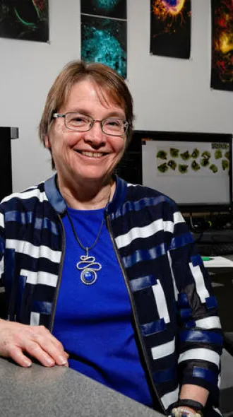 Linda Van Eldik sitting in a computer lab, leaning against a table.