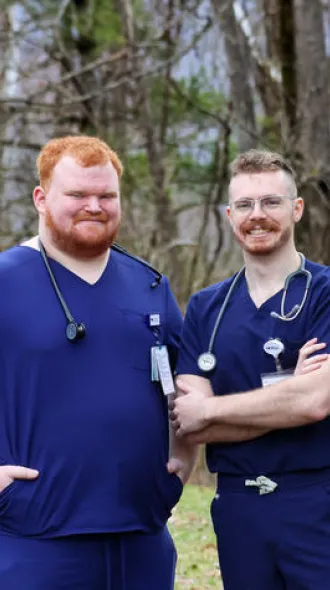 Alex Willett, left, and Bradley Firchow standing in front of a tree line