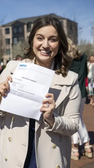 Anna Cox, standing outside, showing off her match letter, while other students talk together in the background.