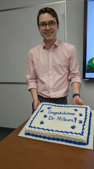 Picture of Dr Milburn holding a cake that says, "Congratulations Dr. Milburn".