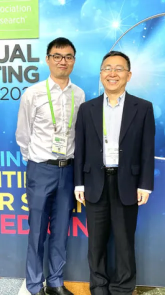 Markey researchers Jinghui Liu and Xiaoqi Liu at the 2023 AACR conference, standing in front of an event banner wall.