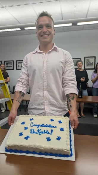 Picture of Dr Keeble holding a cake that says, "Congratulations Dr. Keeble".