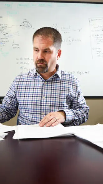 David Fardo, sitting at a desk in front of a white board, sorting through paperwork.