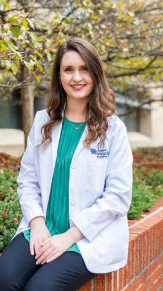 Susanna Goggans, wearing a white coat, sitting on the wall of a garden bed on UK's campus.
