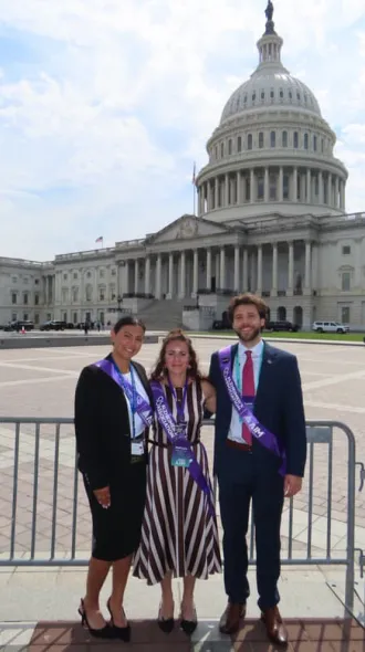 Three students pose together in front of U.S. Capitol Building. Over their clothes, each is wearing a purple sash for Alzheimer's advoacy