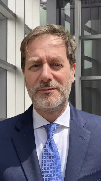 Dr. Pierluigi Porcu stands in a blue suit and blue tie with a white undershirt. He smiles in his headshot.