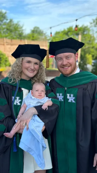 Abigail and Jason Hurt pose in graduation regalia with newborn son, Griffin