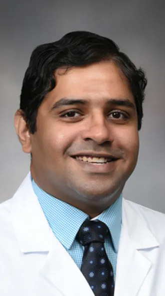 Dr. Paramarajan Piranavan smiles for a headshot. He wears a white coat, blue shirt, and black, patterned tie.