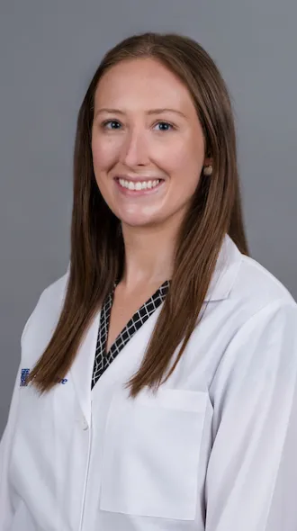 A woman in a white lab coat smiles for a headshot. She has medium length, straight brown hair