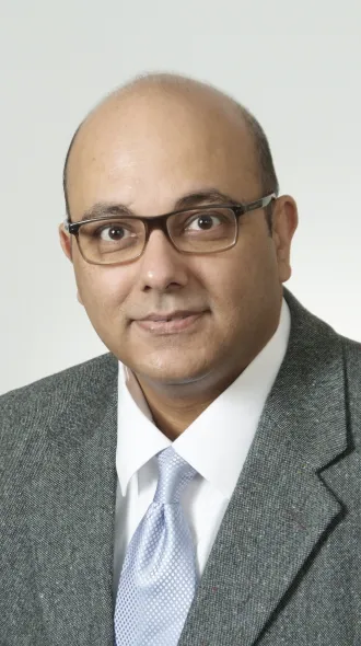A man in a gray sport coat, white shirt, and silky, blue tie smiles for a headshot