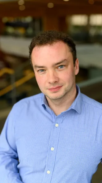 A man poses for a headshot in a blue collared shirt