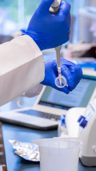 A close up of a lab worker, wearing blue gloves, and prepping a pipette for a centrifuge. 