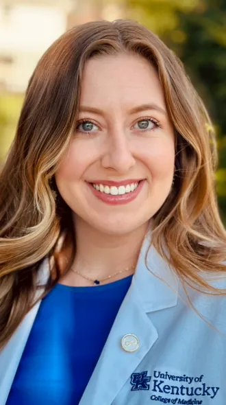 Portrait of Chloe Embry, wearing a blue blouse under a white coat embroidered with UK College of Medicine logo