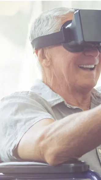 Elder man in wheelchair smiles while wearing a VR Headseat