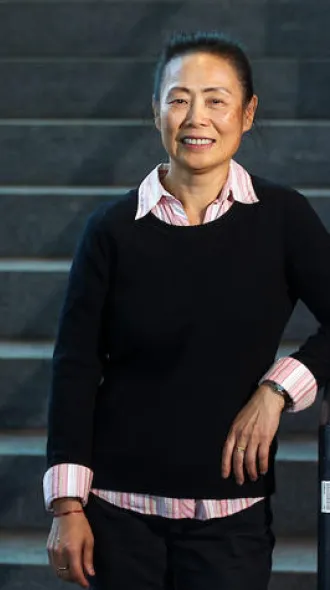 Dr. Wang stands at the bottom of a staircase, wearing a black sweater. 