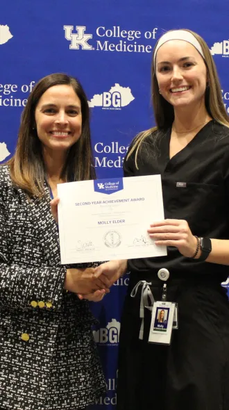 Awardee and presenter hold a certificate and pose for a photo in front of blue backgroudn