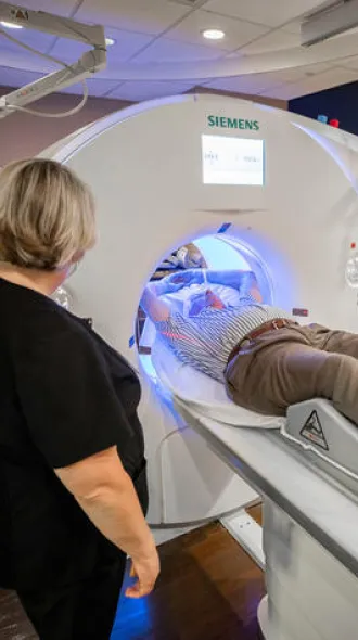 A man receiving a CT scan of his lungs while a female person stands nearby.