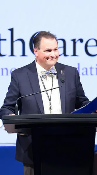 John D'Orazio, MD standing in front of a UK HealthCare Markey Cancer Foundation banner, giving a presentation at a podium.