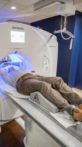 A technician oversees a patient entering a CT scanner in a medical room. The atmosphere appears clinical and focused, with dim lighting and sleek equipment.