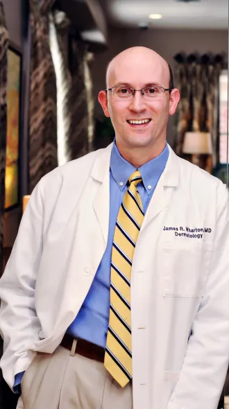 Dr. James Wharton posts for a headshot in a white coat, blue shirt, and striped, yellow tie