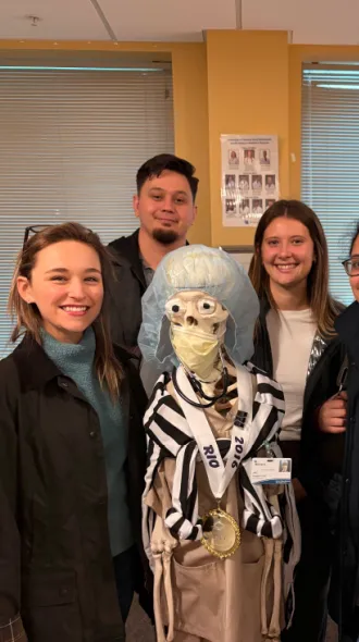 5 medical students pose with a life-size skeleton during a visit to UK COM Morehead Campus