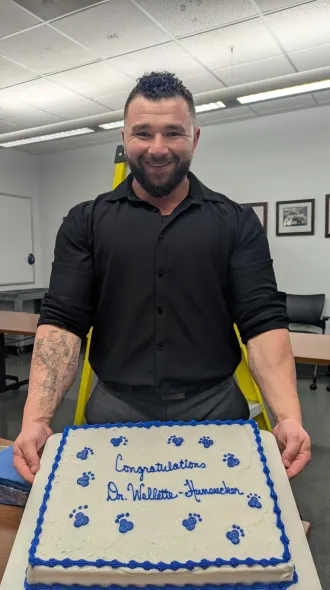 Picture of Dr Wellette-Hunsucker holding a cake that says, "Congratulations Dr. Wellette-Hunsucker".