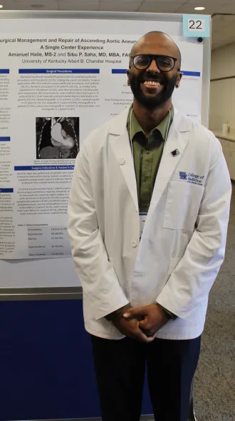Northern Kentucky Campus medical student wearing white coat smiles in front of research poster.