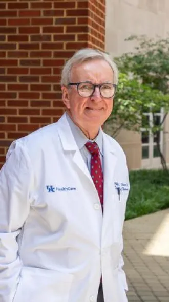 Dr. Phil Tibbs wearing white coat stands in front of brick building for photo
