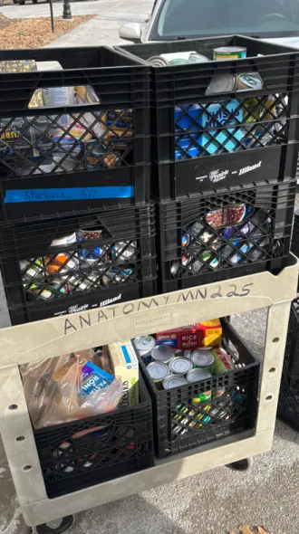 Crates of canned and other non-perishable food collected on a beige wheeled cart to donate. 