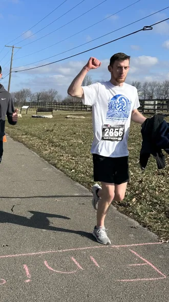 Two men finish a race on a sunny day. The one on the left smiles and gives a thumbs up, while the other raises his arm in triumph. "Finish" is marked on the path.