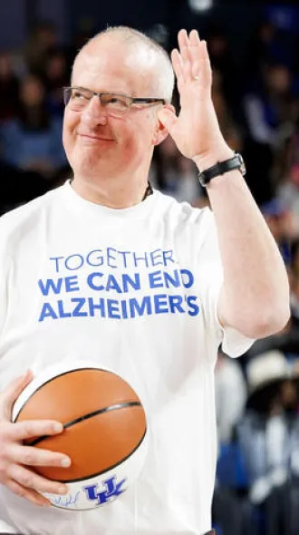 Peter Nelson stands on the UK basketball court, holding a UK basketball and wearing a white shirt that reads, "Together we can end alzheimer's"