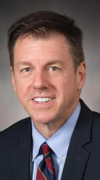 headshot of Dr. Jay Grider, wearing a suit and tie in front of a gray background