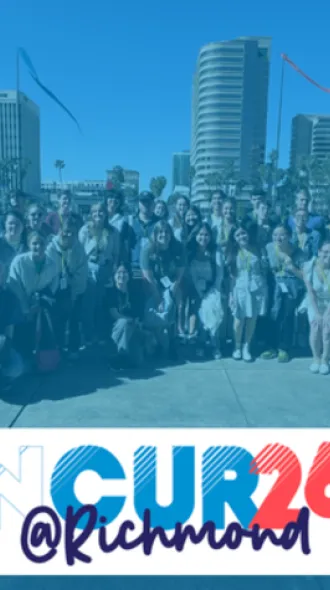 A large group of people pose together outdoors in front of several tall buildings on a sunny day. Streamers or ribbons can be seen in the sky above them. The lower portion of the image contains a white banner with the stylized text “NCUR 26 @ Richmond” in