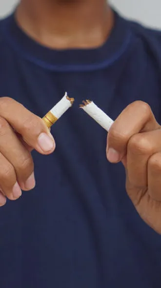 A person in a blue t-shirt snapping a cigarette in half.
