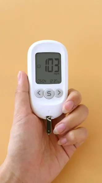 A hand holds up a blood sugar monitor for a diabetic. The monitor reads 103 mg/dL